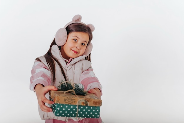 una ragazza in abiti caldi che presenta un regalo sullo sfondo bianco Spazio per il testo