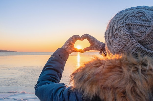 Una ragazza in abiti invernali fa un cuore con le mani nei guanti Sullo sfondo del congelamento