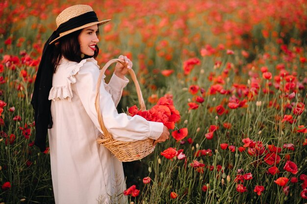 Una ragazza in abito bianco e con un cesto di papaveri cammina in un campo di papaveri