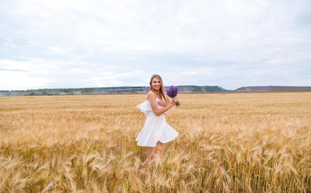 Una ragazza in abito bianco e con un mazzo di lavanda in un campo di grano