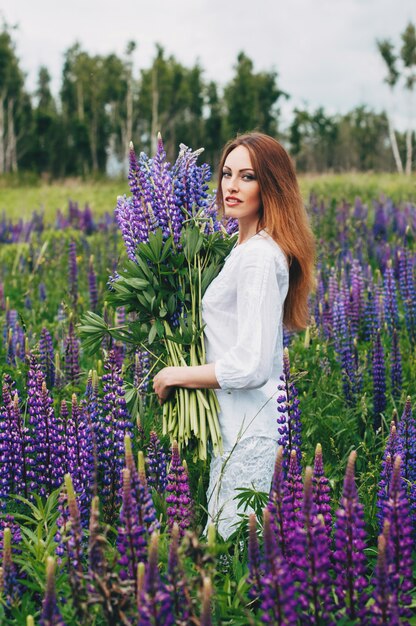 Una ragazza in abito bianco è in piedi tra i lupini