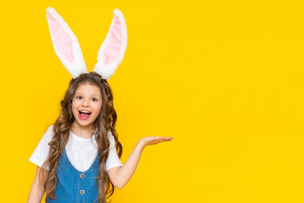 Una ragazza in abito blu con orecchie da coniglio tiene una mano su uno sfondo giallo