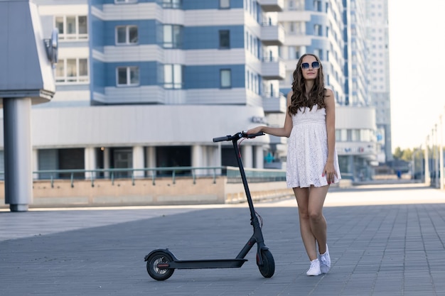 Una ragazza in abito estivo si trova accanto a uno scooter elettrico in città