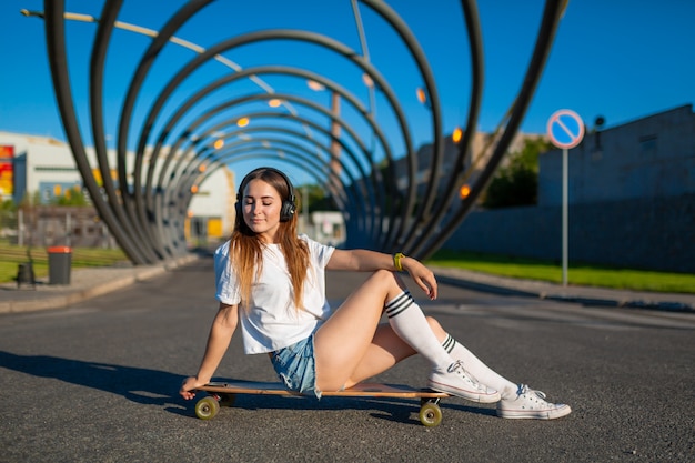 Una ragazza in berretto da baseball si siede su skateboard, longboard.