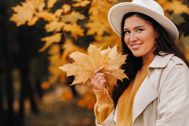 Una ragazza in camice bianco e cappello sorride in un autunno Park.Ritratto di una donna in autunno dorato.