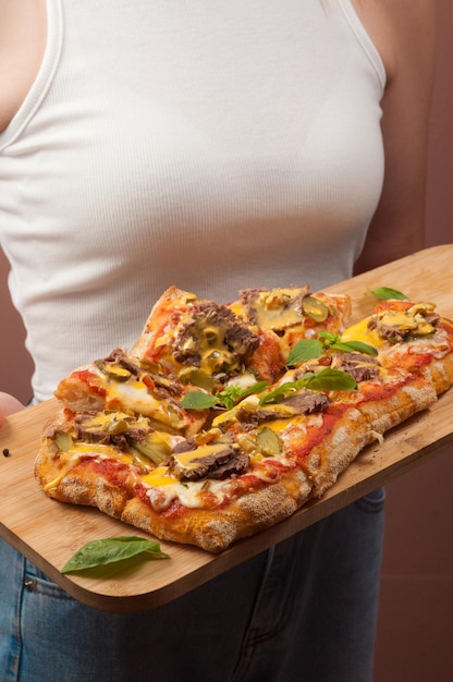 Una ragazza in canottiera bianca tiene in mano una pizza italiana