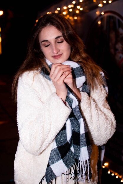 Una ragazza in cappotto e guanti sta sotto un albero di Natale decorato con luci. Capodanno 2022.