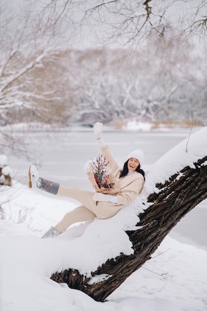 Una ragazza in cardigan beige e fiori invernali cammina nella natura nella stagione nevosa Tempo invernale