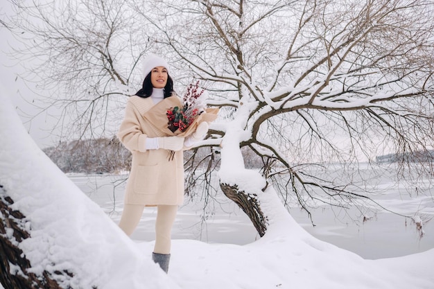 Una ragazza in cardigan beige e fiori invernali cammina nella natura nella stagione nevosa Tempo invernale