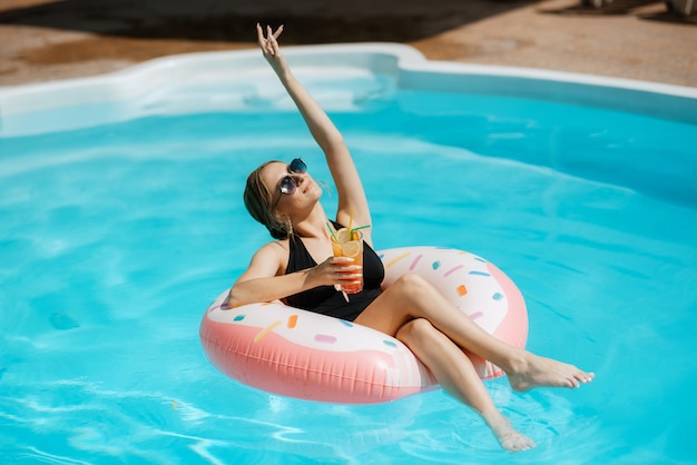 Una ragazza in costume da bagno nero galleggia in una piscina blu