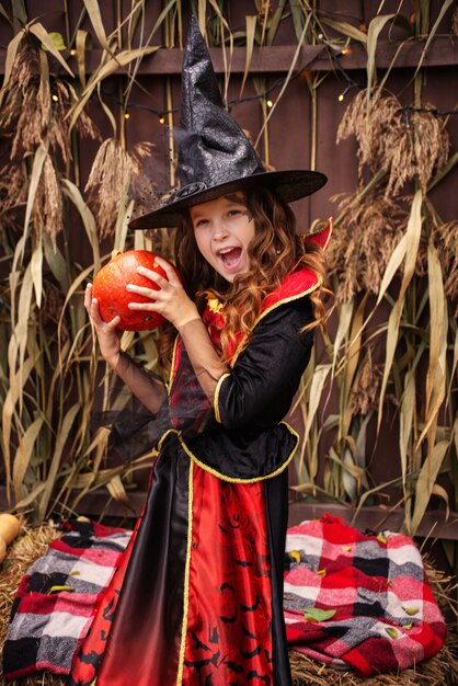 una ragazza in costume da strega lancia una magia su una zucca di halloween