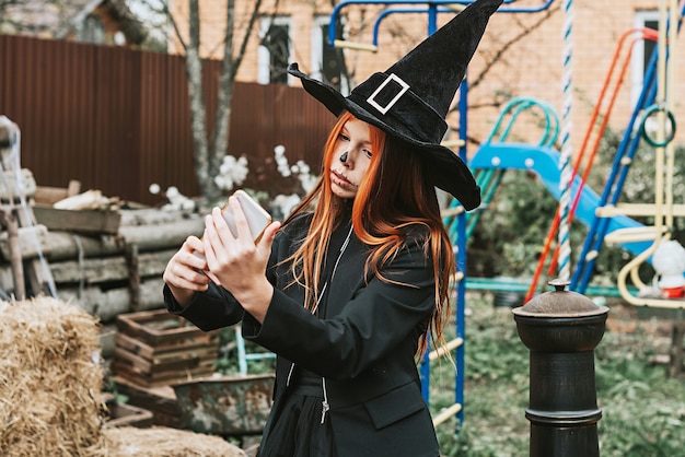 Una ragazza in costume da strega si fa un selfie a una festa di Halloween sotto il portico decorato