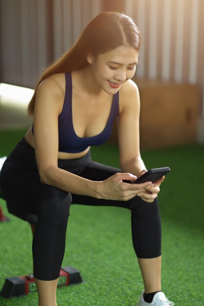 Una ragazza in forma sana si siede nel centro benessere utilizzando un telefono cellulare moderno. bella donna in abbigliamento sportivo utilizzando smartphone.