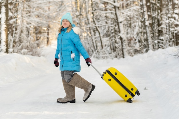 Una ragazza in inverno con stivali di feltro va con una valigia in una gelida giornata di neve.