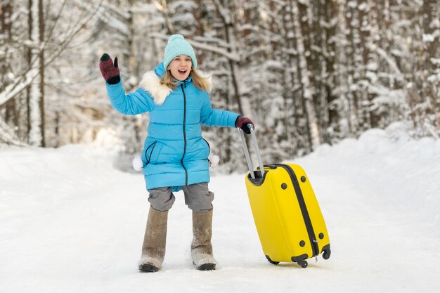 Una ragazza in inverno con stivali di feltro va con una valigia in una gelida giornata di neve