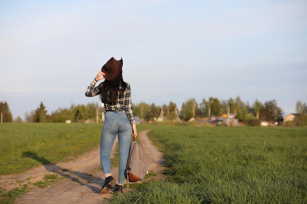 Una ragazza in jeans e cappello viaggia l'estate in campagna