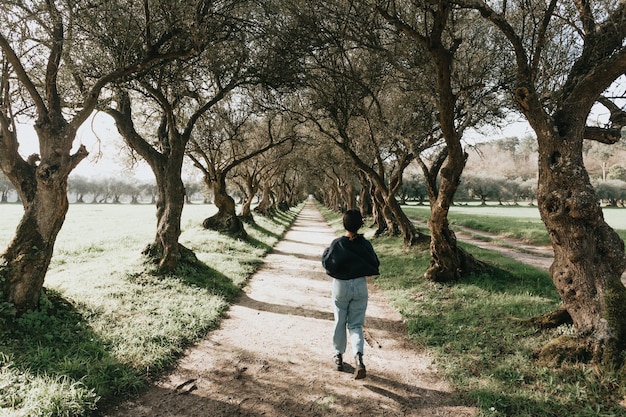 Una ragazza in jeans e stile hipster corre tra i filari di piantagioni di ulivi. Immagine in stile film indipendente, libertà, libertà e concetto futuro. Vibrazioni di vita giovane che sognano un'immagine reale naturale.