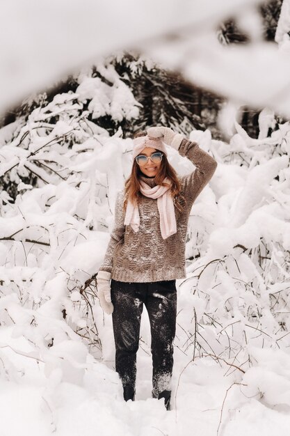 Una ragazza in maglione e occhiali in inverno in una foresta innevata