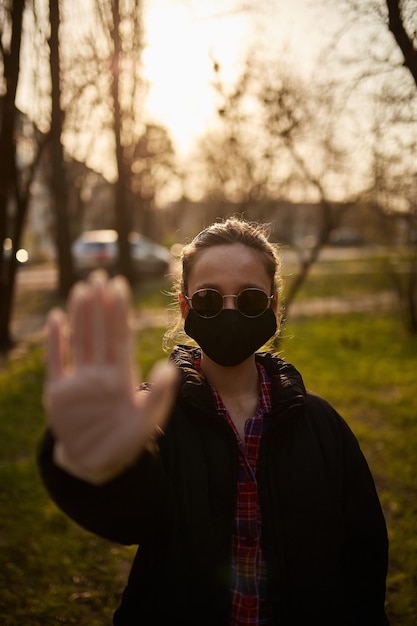 una ragazza in maschera medica nera mostra con la mano il segnale di STOP