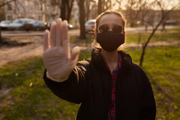 una ragazza in maschera medica nera mostra con la mano il segnale di STOP