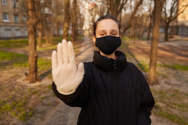 una ragazza in maschera medica nera mostra con la mano il segnale di STOP