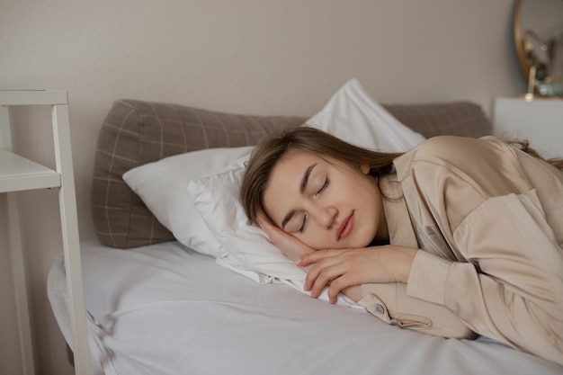 Una ragazza in pigiama beige dorme su un letto bianco.
