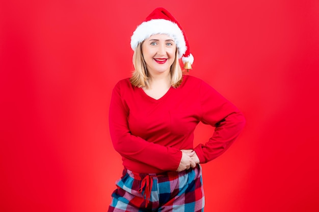 Una ragazza in pigiama di Natale e un cappello di Babbo Natale su uno sfondo rosso