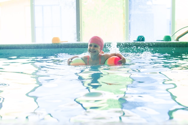 Una ragazza in piscina raccoglie palline colorate. Allenamento di nuoto