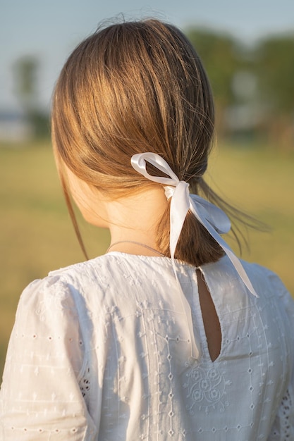 Una ragazza in stile rustico Nastro bianco tra i capelli biondi Una ragazza in un abito bianco sta con le spalle alla telecamera