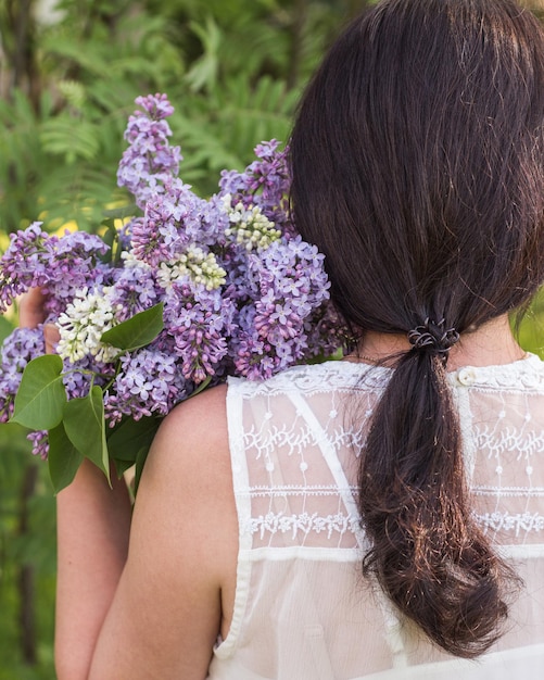 Una ragazza in un abito bianco abbraccia un mazzo di lillà Un mazzo di lillà sulla spalla di una donna