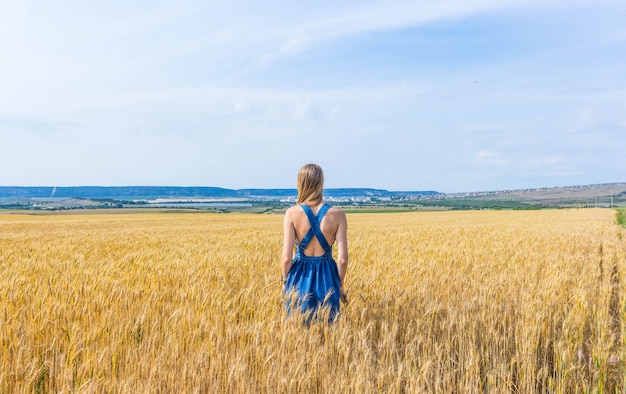 Una ragazza in un abito blu in piedi su un campo di grano