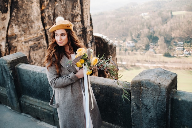 Una ragazza in un abito rosa e un cappello con un mazzo di fiori sullo sfondo di montagne e gole in Svizzera Sassonia, Germania, Bastey.