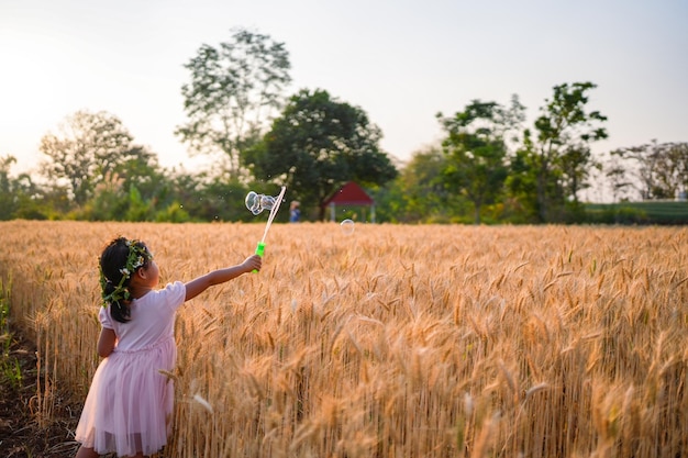 Una ragazza in un campo di grano soffia bolle