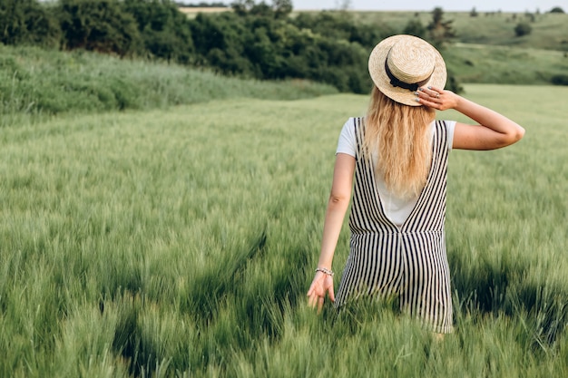 Una ragazza in un cappello di paglia cammina su un campo verde al tramonto