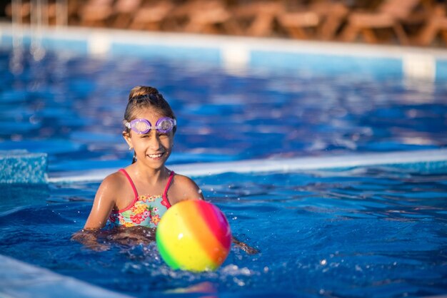 Una ragazza in un costume da bagno luminoso nuota con una palla gonfiabile in una piscina con acqua limpida in una sera d'estate