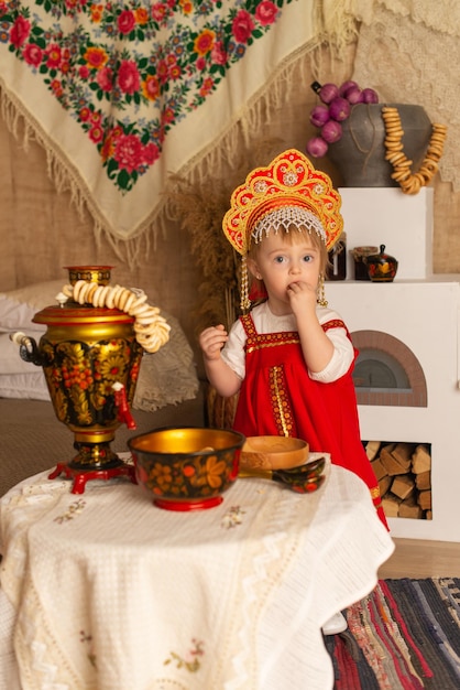 Una ragazza in un costume nazionale rosso vicino a un tavolo con un samovar e volanti Pancake day