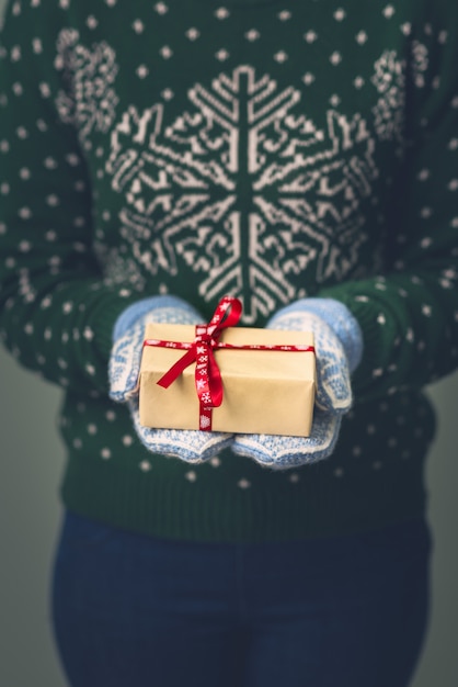 Una ragazza in un maglione di Capodanno tiene un regalo. Regali per uomini. Buon Natale. Regalo per una ragazza Maglione con ornamento di Natale. Abito in maglia