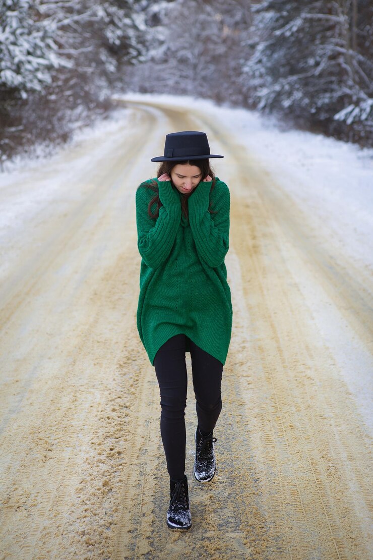 Foto una ragazza in un maglione verde si trova nel mezzo di una strada innevata in una fitta foresta di pini f