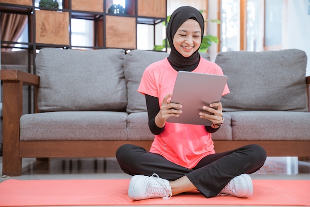 Una ragazza in un vestito da palestra di velo con un sorriso guardando un tablet dopo l'esercizio al coperto a casa