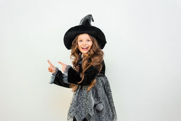 Una ragazza in un vestito da strega indica un annuncio Una bella maga su uno sfondo isolato Vestito di Halloween del mago