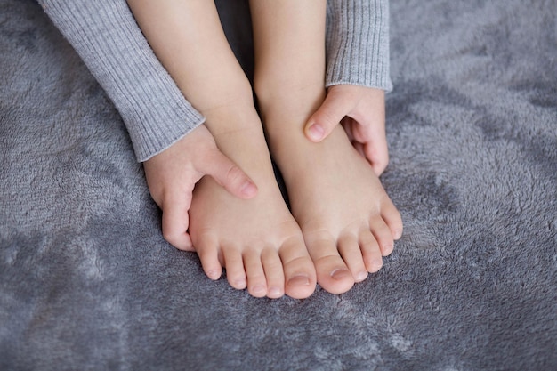 Una ragazza in un vestito grigio tiene le gambe con le mani su uno sfondo grigio primo piano Giochi per bambini ragazza