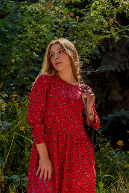 Una ragazza in un vestito rosso con i capelli lunghi su uno sfondo di verde in estate. bella ragazza in natura