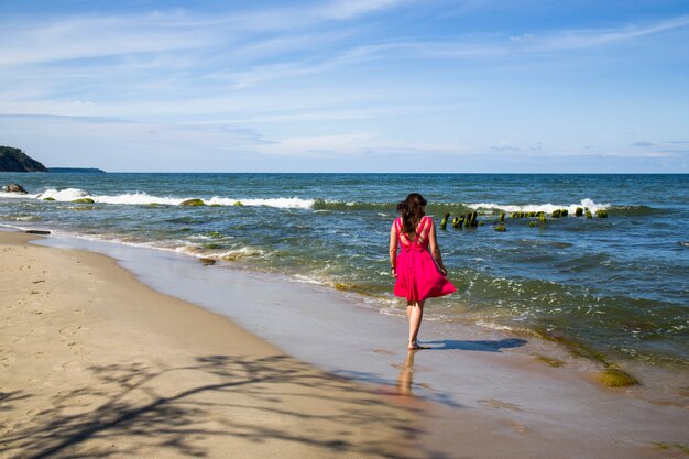 Una ragazza in un vestito scarlatto in riva al mare. Vento, onde, spiaggia deserta. Una vacanza al Sud