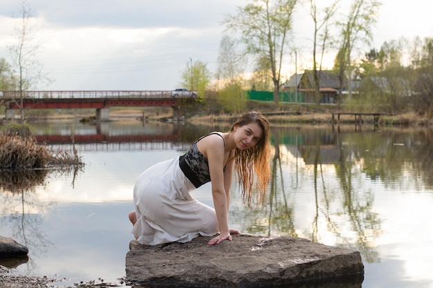 Una ragazza in un vestito su una pietra nel fiume con un riflesso del cielo con le nuvole nell'acqua