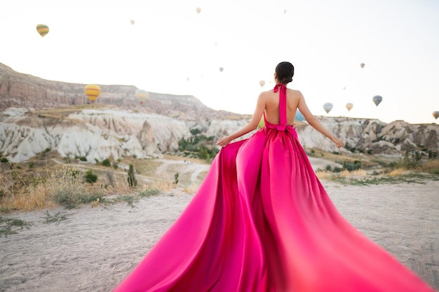 Una ragazza in un vestito volante con un lungo strascico sullo sfondo di palloncini in Cappadocia