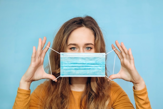 Una ragazza in una maglietta gialla indossa una maschera medica. Ritratto di un primo piano biondo su sfondo blu in una maschera protettiva. Protezione dal coronavirus. covid-2019. pandemia 2020.