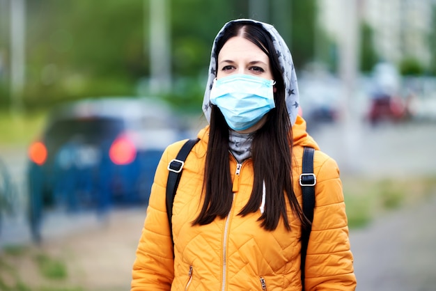 Una ragazza in una maschera medica, cappuccio e valigetta, guardando avanti, in futuro. Ehi con una giacca arancione