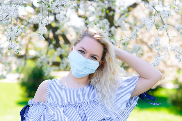 Una ragazza in una maschera medica protettiva in primavera tra il giardino fiorito. . Allergia primaverile e concetto covid.