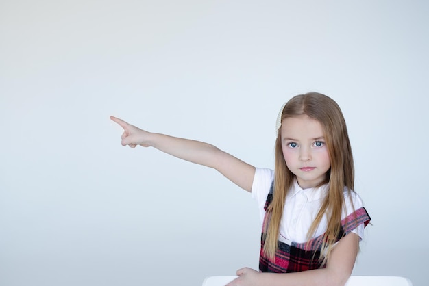 una ragazza in uniforme scolastica su sfondo bianco punta il dito nel vuoto
