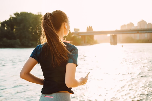 Una ragazza in uniforme sportiva esegue una corsa serale con un telefono in mano